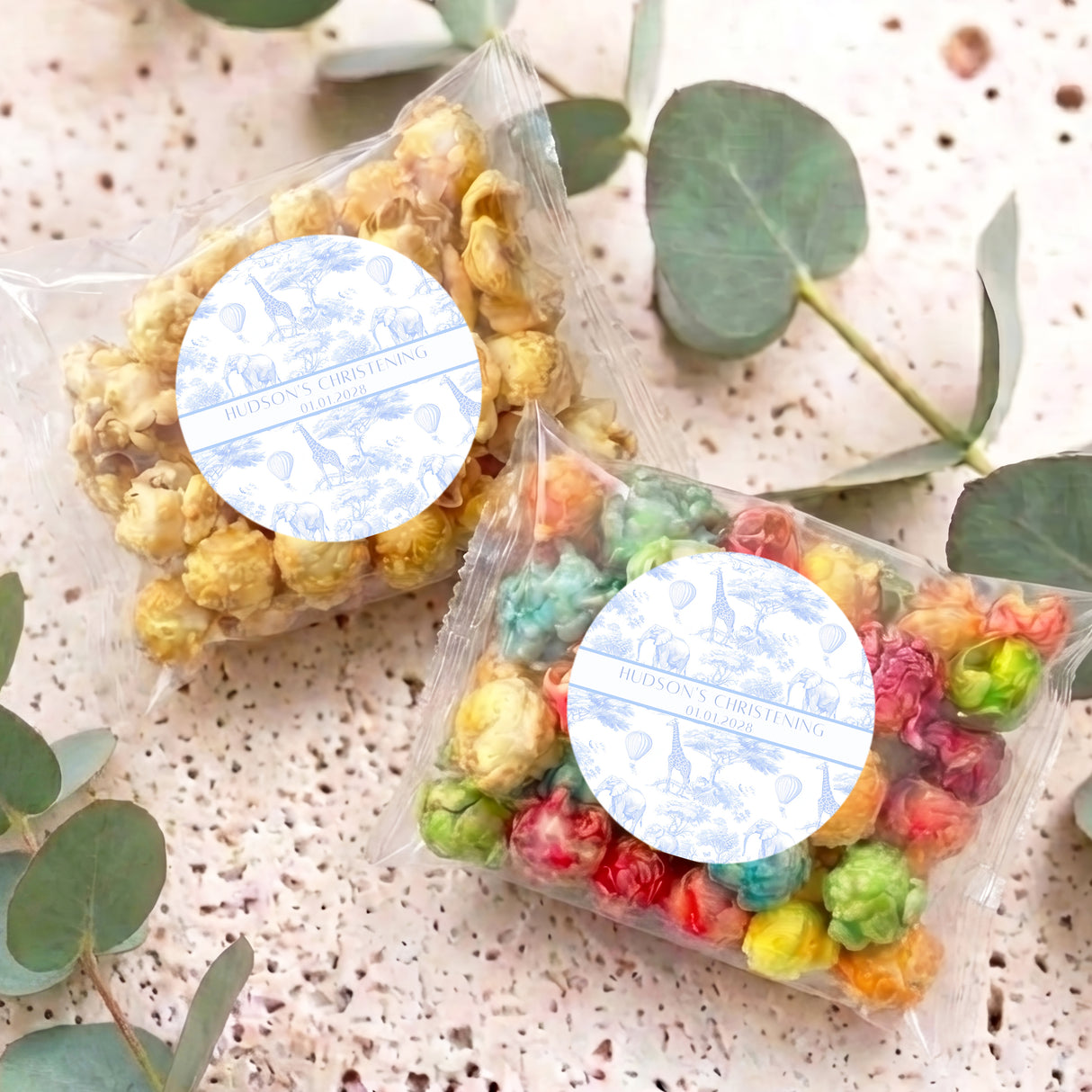 Two personalised popcorn favor bags with blue round labels, clear bags of colorful popcorn