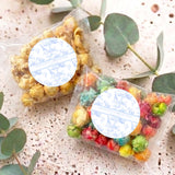 Two personalised popcorn favor bags with blue round labels, clear bags of colorful popcorn