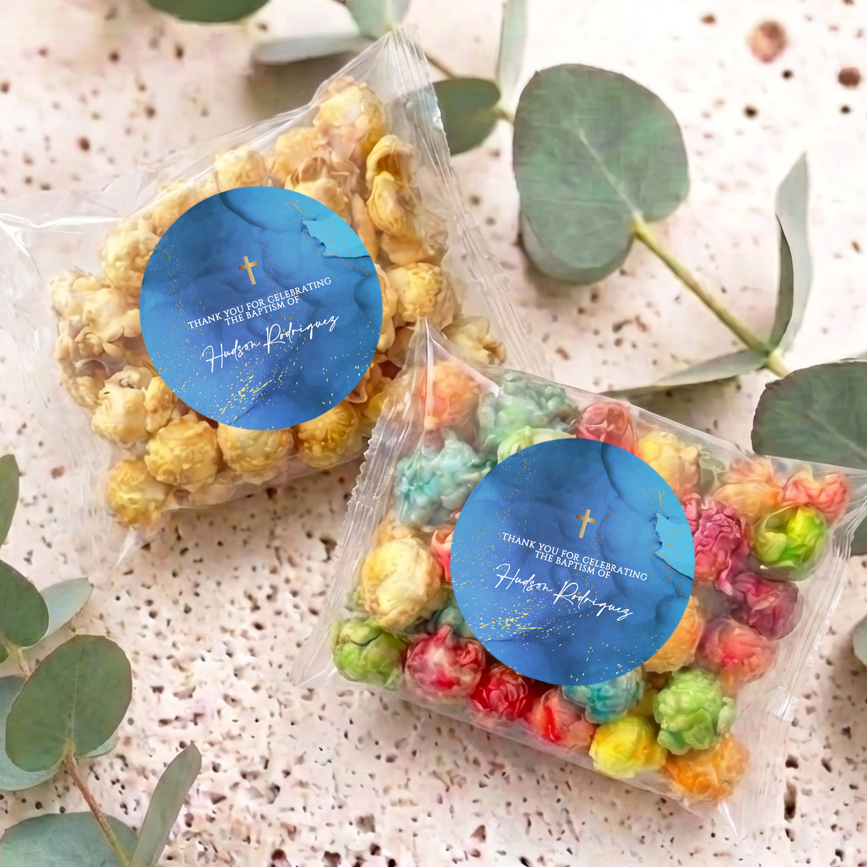Two personalised popcorn bags in clear wrap with blue Christening labels on table