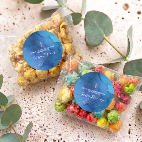 Two personalised popcorn bags in clear wrap with blue Christening labels on table