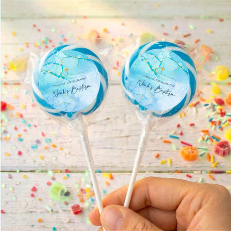 Personalised blue baptism lollipops with gold cross design on clear wrappers, held in hand