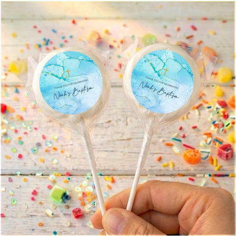Two blue personalised baptism lollipops on clear sticks, gold cross motif visible on wrapped tops