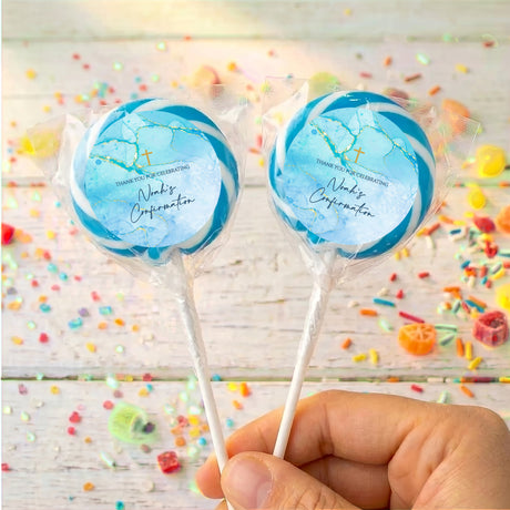 Two blue personalized lollipops in clear wrappers with gold cross, held in hand