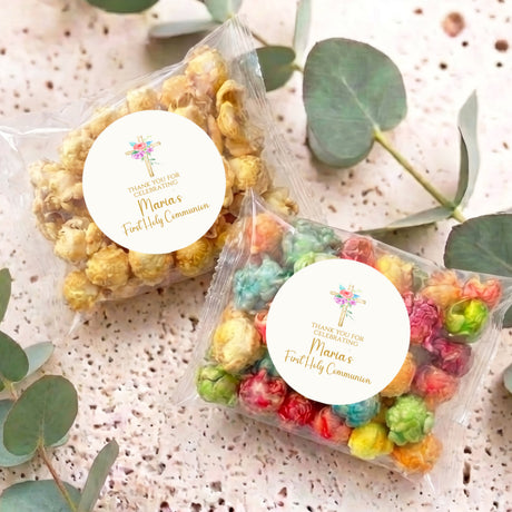 Personalised popcorn bags with floral holy cross thank-you labels on table