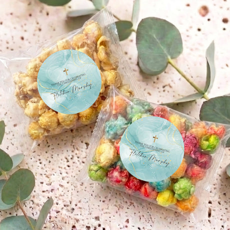 Personalised popcorn bag with blue round label and multicolour popcorn, lying flat.