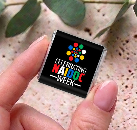 Mini chocolate box held between fingers, black 'Celebrating NAIDOC WEEK' label