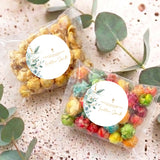 Personalised popcorn bags with round leaf-and-gold cross labels, on speckled surface