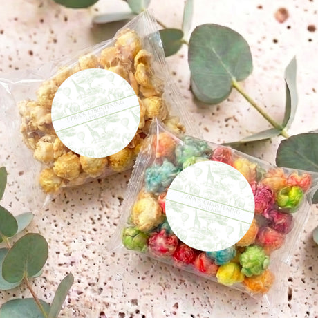 Two clear popcorn gift bags with colorful mini puffs and round white personalized labels