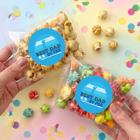 Hands holding personalized clear plastic popcorn bags with blue Best Dad By Par labels