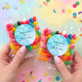 Two personalised jelly bean pouches with blue labels and multicolored candies held by hands