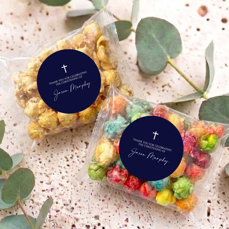 Popcorn favor bags with navy round labels and white cross, filled with pastel popcorn.