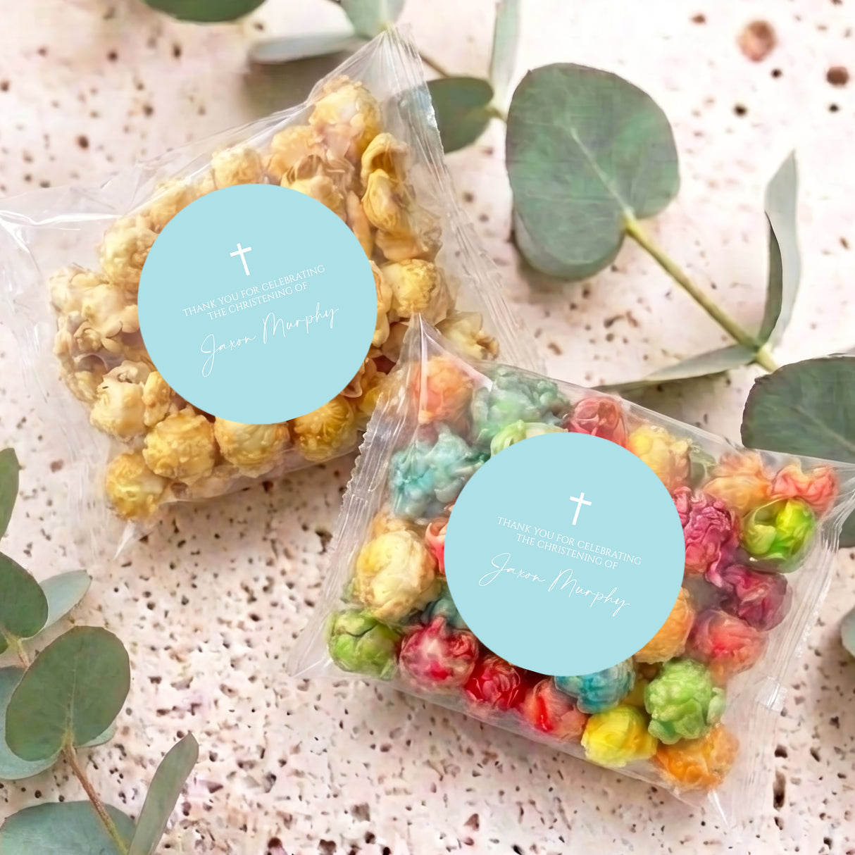 Pastel blue christening popcorn bags on table, clear bags with popcorn and turquoise cross tags