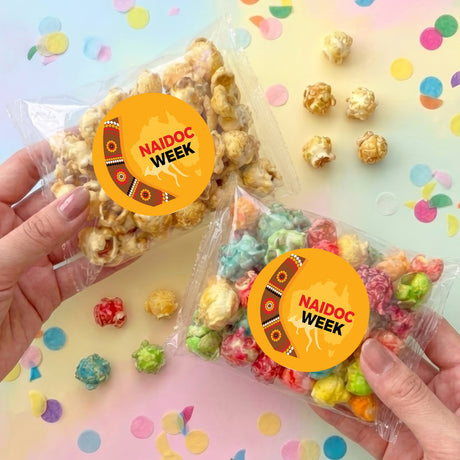 Personalised popcorn bag held in hands, clear bag with pastel popcorn and orange Naidoc Week label