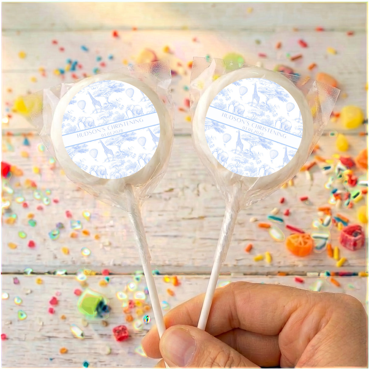 Personalised christening lollipop with white printed wrapper, two on sticks held by hand