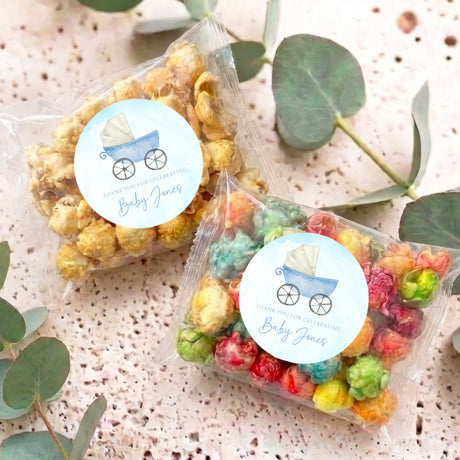 Personalized popcorn bags with round baby-themed labels, filled with colorful popcorn