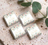 Set of four mini chocolate favor boxes with cream floral roses wrappers and eucalyptus leaves