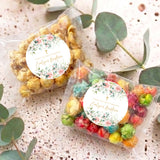 Pair of transparent popcorn bags with floral baptism labels and mixed pastel popcorn