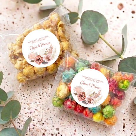 Personalised popcorn bag pair with clear wrappers and pink floral round labels; flat lay
