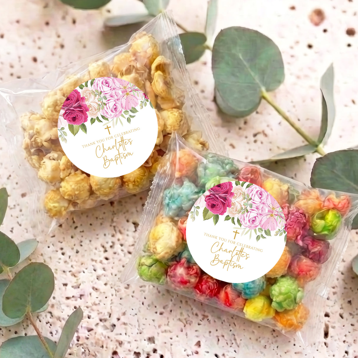Two clear popcorn gift bags with colorful popcorn and round pink rose personalized labels