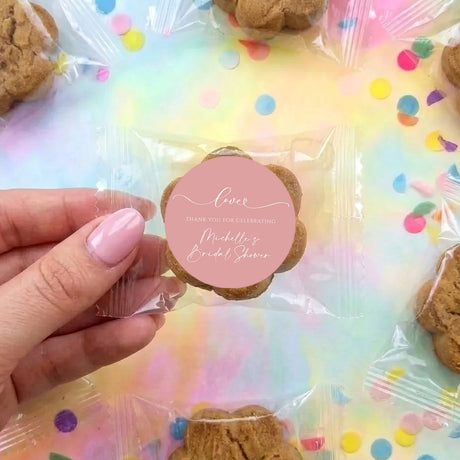Hand holding round cookie with pink custom sticker on clear treat bag