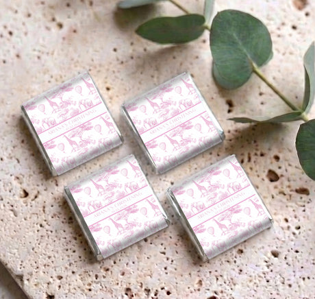 Mini chocolates with pink safari-pattern foil wrappers arranged on a surface with eucalyptus leaves