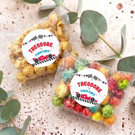 Two personalised popcorn bags with colorful kernels and round race-car labels reading Theodore