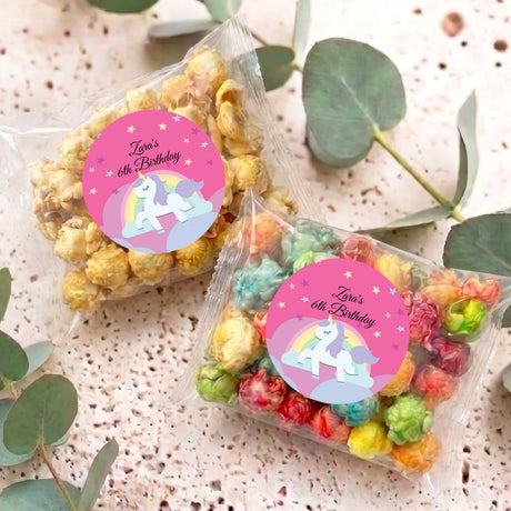 Two personalised unicorn birthday popcorn bags with pink 'Zara's 6th Birthday' labels