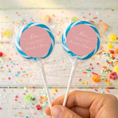 Personalised dusty pink lollipops with blue-edged wrappers, round love labels, held in hand