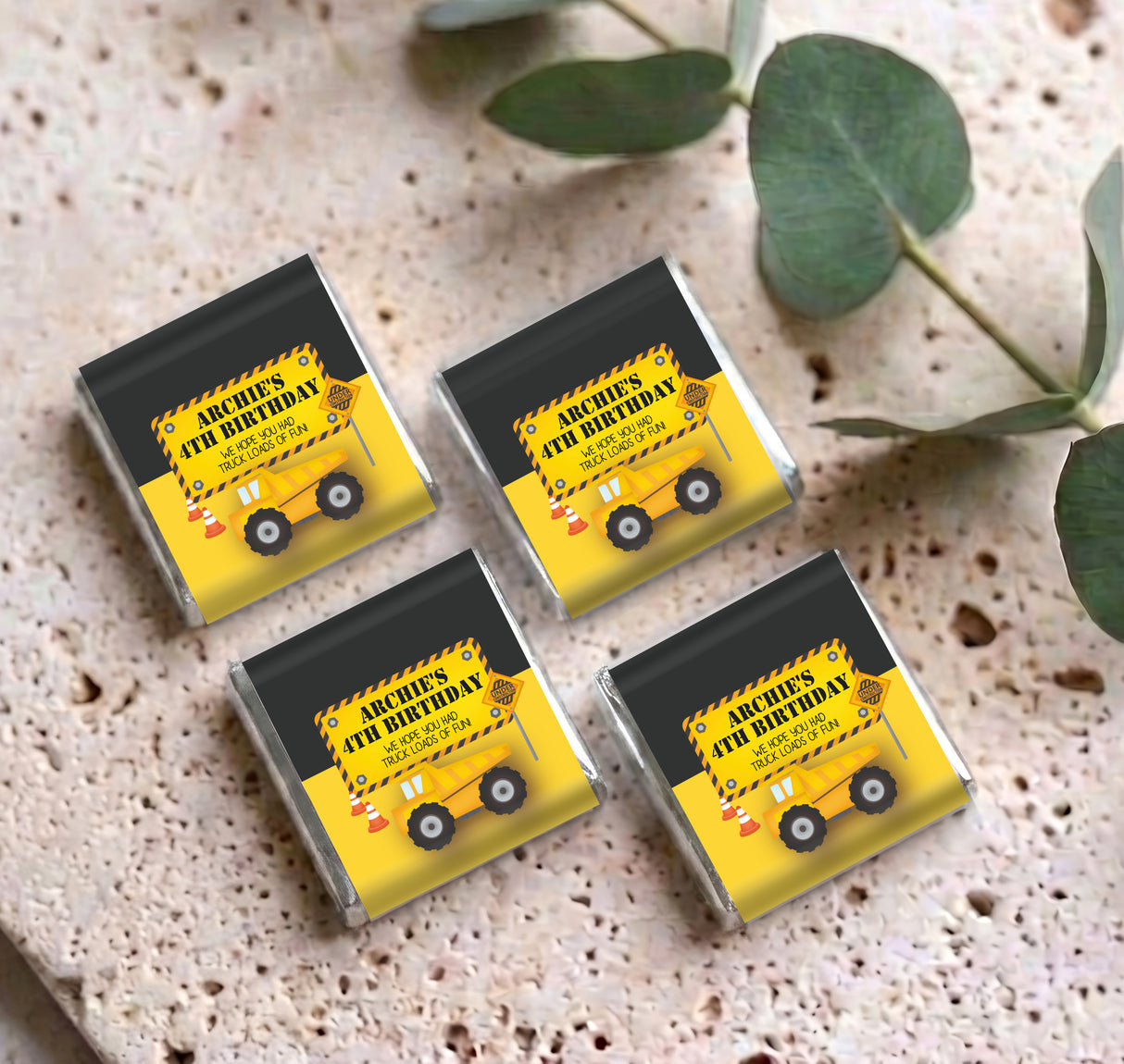 Four personalised mini chocolate bars with yellow truck birthday wrappers on speckled paper