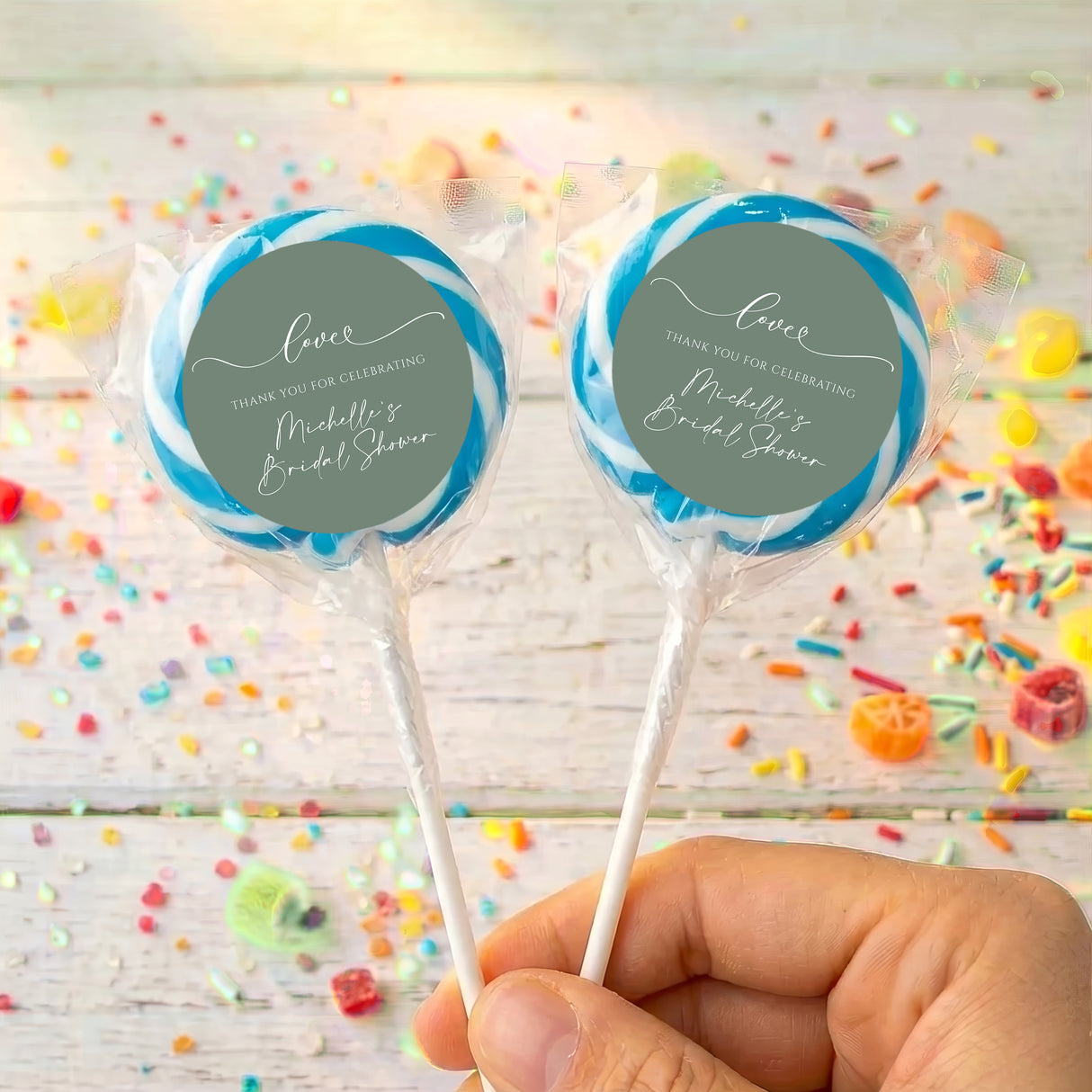 Personalised wrapped lollipops with round sage-green labels and blue ribbon accents on sticks