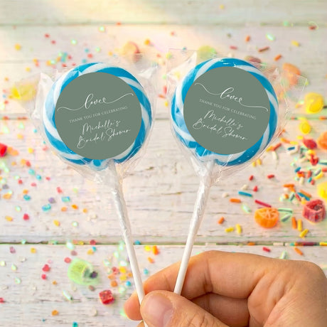 Personalised wrapped lollipops with round sage-green labels and blue ribbon accents on sticks
