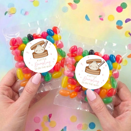 Pair of clear jelly bean bags with round label, filled with mixed-color candies, held