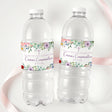 Printed bottle labels on two clear soda bottles with wildflower band and red accents