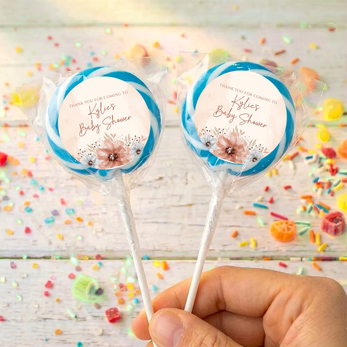 Baby shower lollipop pair with blue foil rings and floral thank-you labels, held in hand
