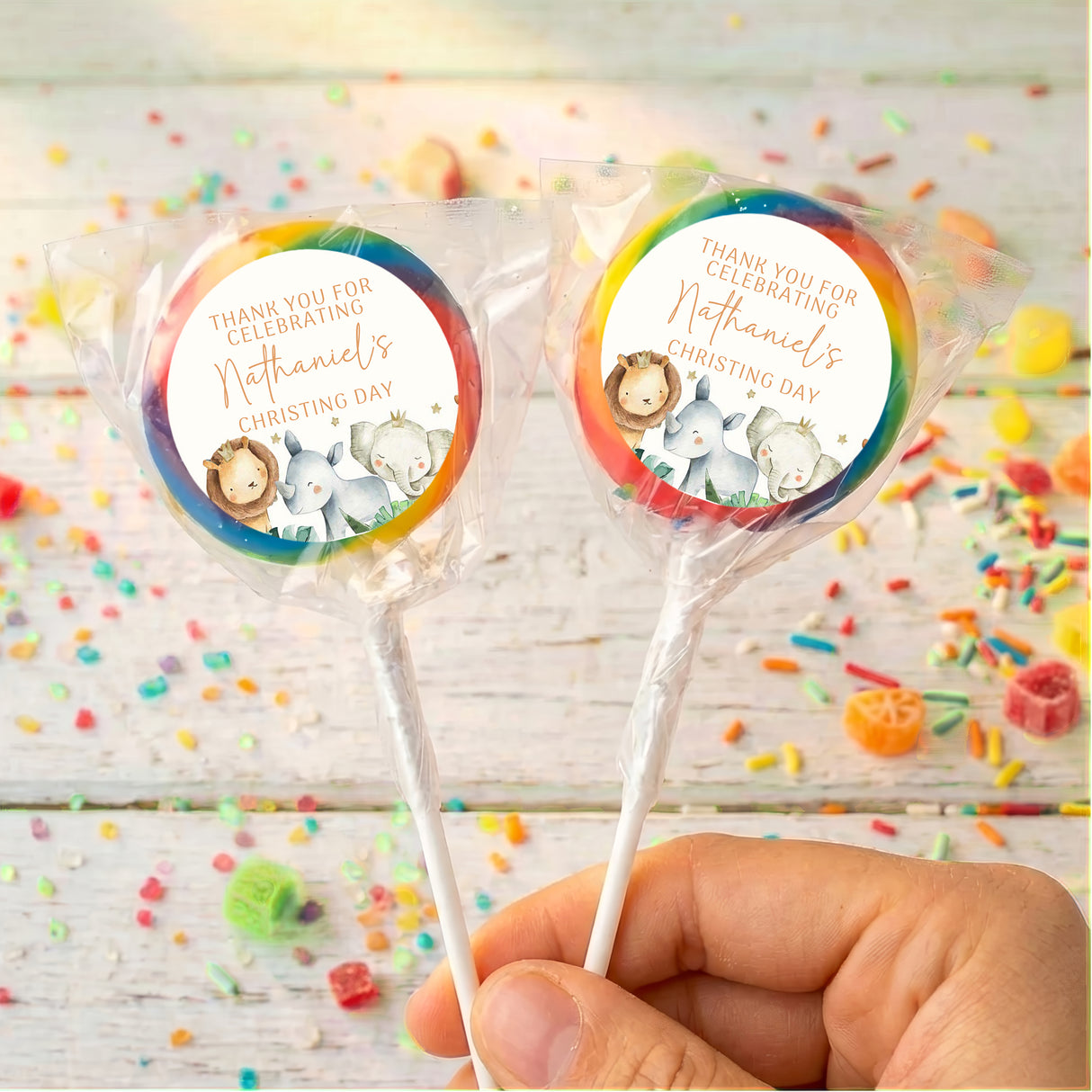 Christening lollipops with clear wrappers and rainbow watercolor baby animal circle labels, hand-held