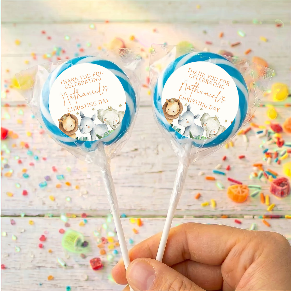 Christening lollipops with clear wrappers and blue watercolor baby animal circle labels, hand-held