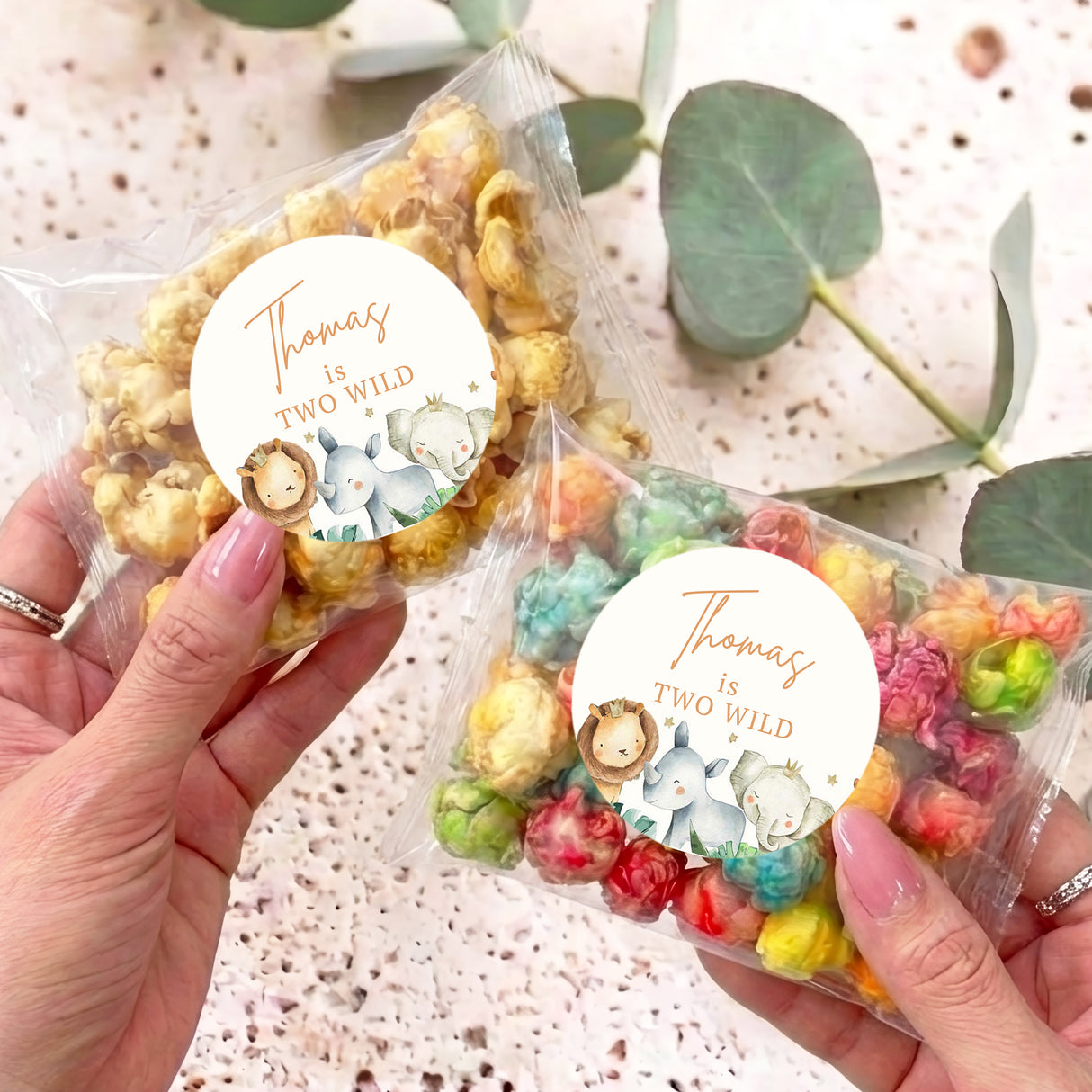 Personalised clear popcorn bag with round sticker label and watercolor baby animals, held in hand