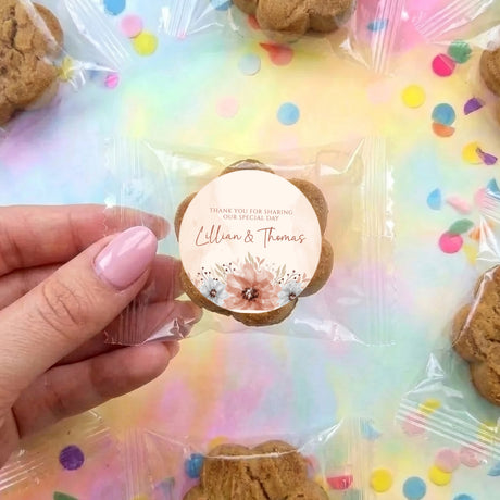 Personalised bite-size choc chip cookie with round thank-you sticker held by a hand