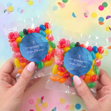 Two personalised jelly bean bags in clear wrappers with blue cross labels, held in hands