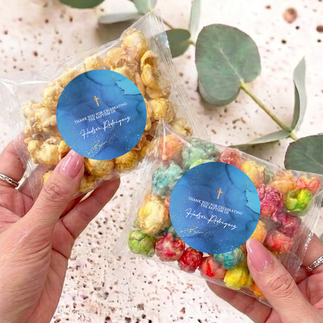 Personalised popcorn bag in clear wrap with blue Christening label, held in hand