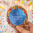 Round blue thank-you sticker with gold cross, in clear sleeve with colorful bead border