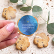 Hand holds bite-size chocolate chip cookie with blue First Communion gold cross label