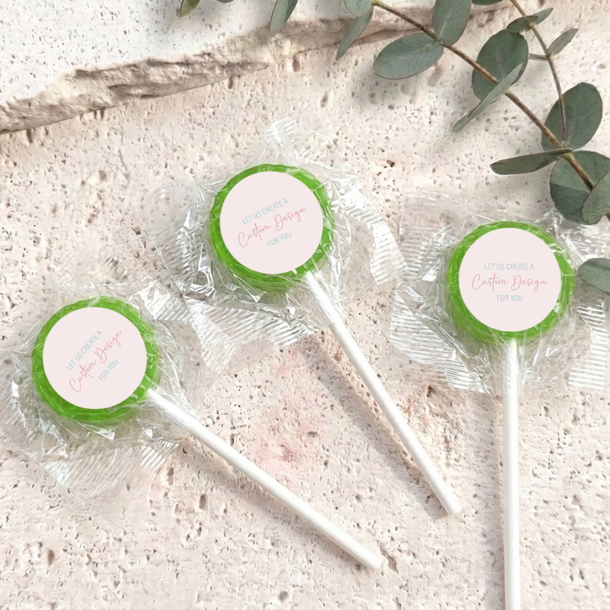 Mini lollipops with green lollipop tops, wrapped in clear plastic on white sticks.
