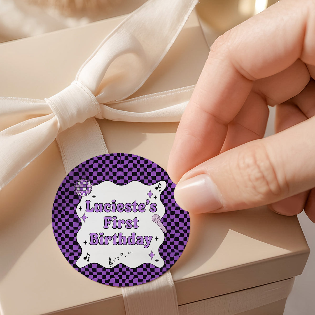 Purple checked round birthday label on white satin ribbon bow: Luciest's First Birthday