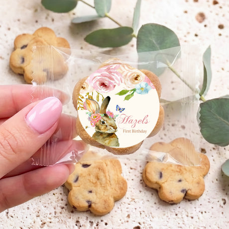 Hand holding personalised floral bunny first birthday choc chip cookie in clear wrapper