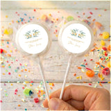 Baptism personalised lollipops with floral cross round labels, clear wrappers, held by hand.