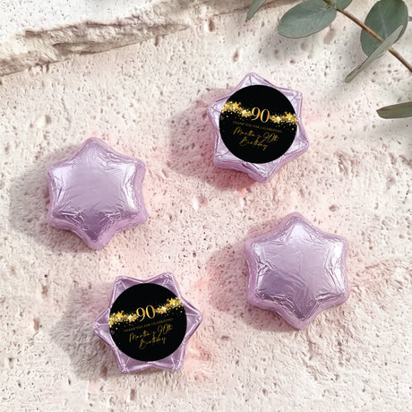 Foil-covered chocolate star sweets in lilac with round “90” black and gold label.