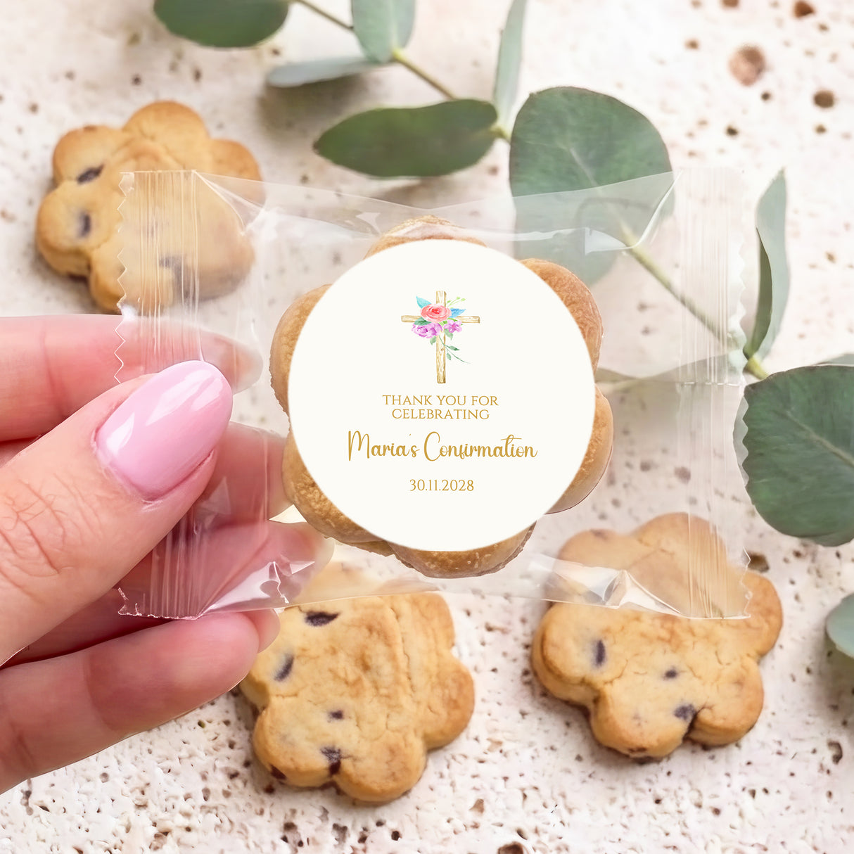 Hand holding cookie with round Marian's Confirmation label, floral holy cross, 30.11.2028