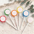 Mini lollipops with multicolor tops—green, orange, yellow, blue, and red—wrapped on sticks.