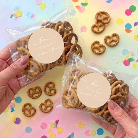 Personalised pretzel bags with clear plastic packaging and beige labels, filled with pretzels.